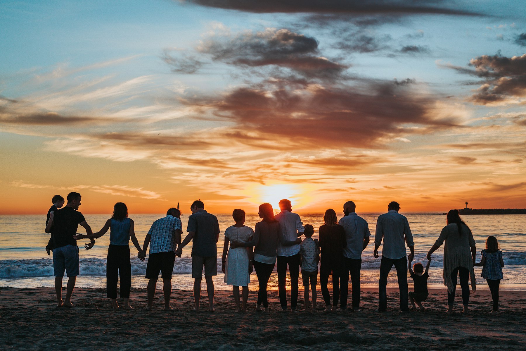An extended family holding hands on a beach at sunset