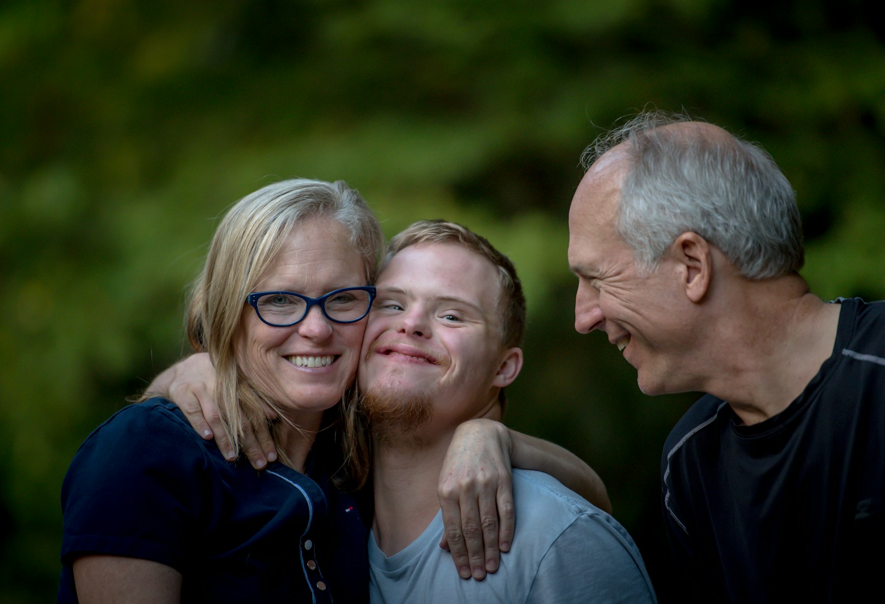 Parents embracing their smiling adult son outdoors, cheek to cheek
