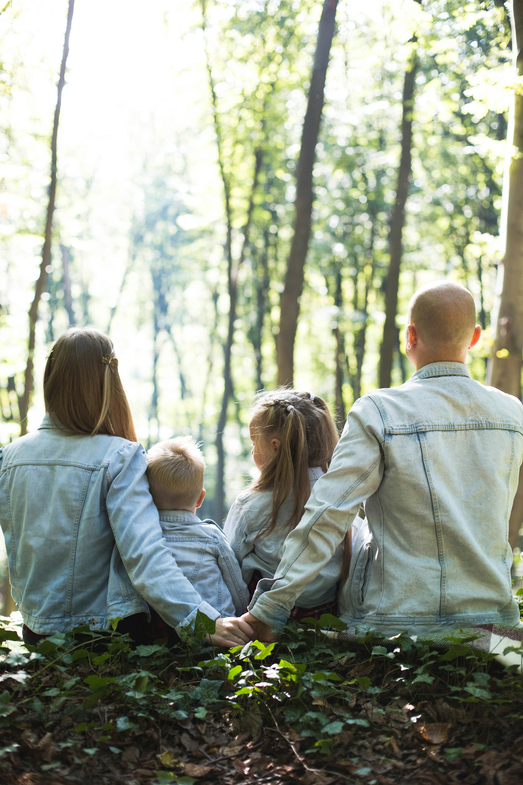 Parents and their two children sitting close together in dappled woodland light