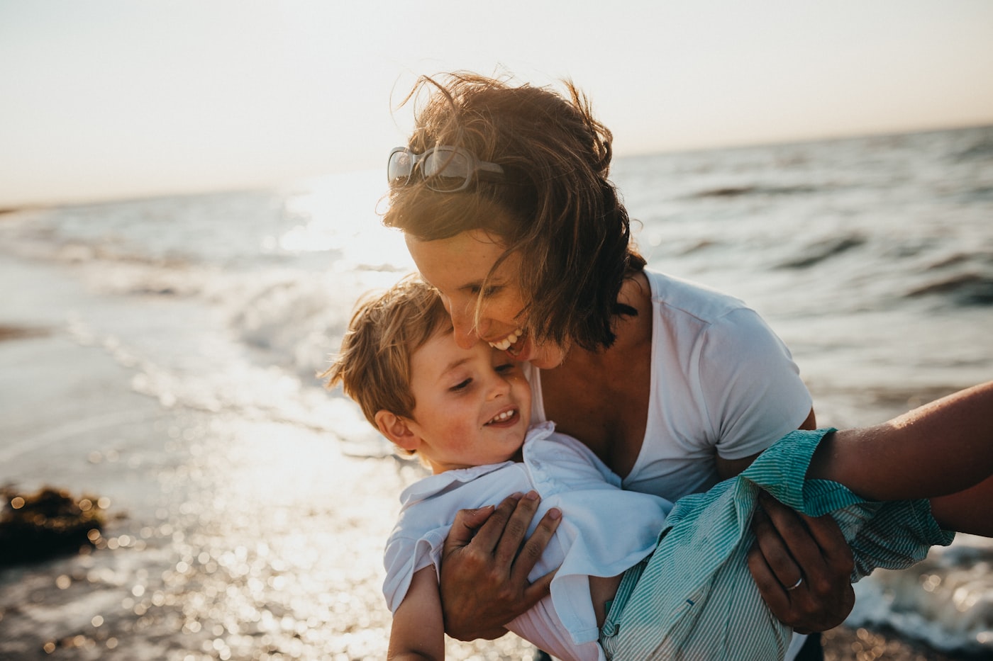A mother holding her young son close and smiling, on the beach at sunset